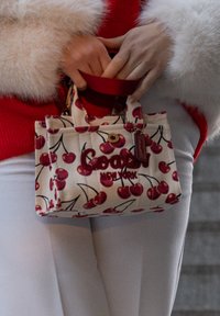 Canvasväska med körsbärstryck i rött och rosa, med en röd logo "Goofy New York" och ett kort handtag.