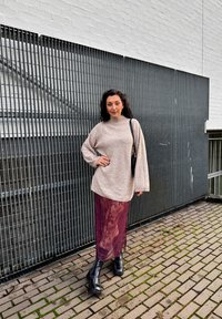 Suéter oversized creme de malha com mangas longas, combinado com uma saia de renda burgundy transparente e botas ankle pretas sobre uma superfície de calçada.