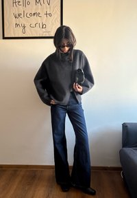 Pull gris surdimensionné à col montant, associé à un jean évasé foncé. Accessoires : un petit sac noir et des lunettes de soleil.