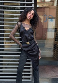 Sort satin top med blondeaccent, lag-på-lag over en gennemsigtig mesh langærmet skjorte. Kombineret med bukser med nålestriber og et bælte med logohardware.