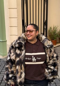 Manteau en fausse fourrure à imprimé léopard avec un col montant, associé à un polo marron foncé avec un logo à rayures blanches. Accessoires : boucles d'oreilles dorées.