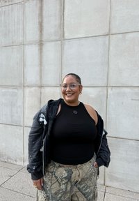 Must have mustel võiava tumedat tank top, liiga suur tume kapuutsiga jope, millel on kerge pritsmega mustus, ja kamuflaažipüksid värvipriipudega; selged prillid ja hõbedased aksessuaarid.