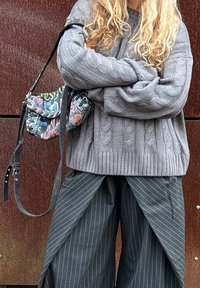 Pull gris en maille torsadée avec manches surdimensionnées et ourlet côtelé, associé à un pantalon large rayé noir et un sac bandoulière graphique multicolore.