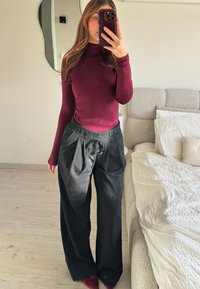 Bordeaux langærmet top sat sammen med sorte højtaljede, plisserede bukser. Outfittet har en glat tekstur og en afslappet pasform.