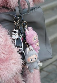 Bolsa de couro cinza com pompom rosa, boneca de pelúcia cinza vestida de coelho, boneca de pelúcia rosa e óculos de sol anexados.
