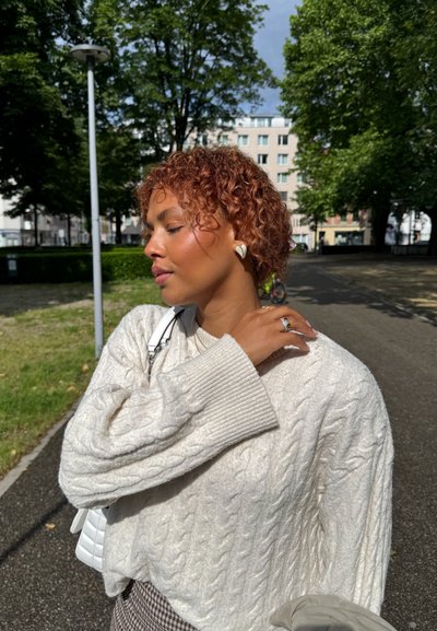 Suéter de punto trenzado crema, pendientes en forma de corazón y pantalones de cuadros. Los detalles notables incluyen tejido texturizado y accesorios de plata.