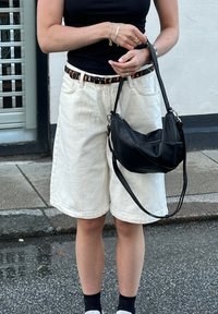 Κρεμ denim σορτσάκια με γυρισμένα τελειώματα, συνδυασμένα με μαύρη δερμάτινη τσάντ�α ώμου και μαύρα υποδήματα με λευκές σόλες.