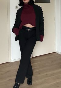 Blazer noir sur un col roulé bordeaux, assorti à un pantalon noir et des chaussures noires. Les caractéristiques comprennent une ceinture avec un accent métallique et des poches latérales.