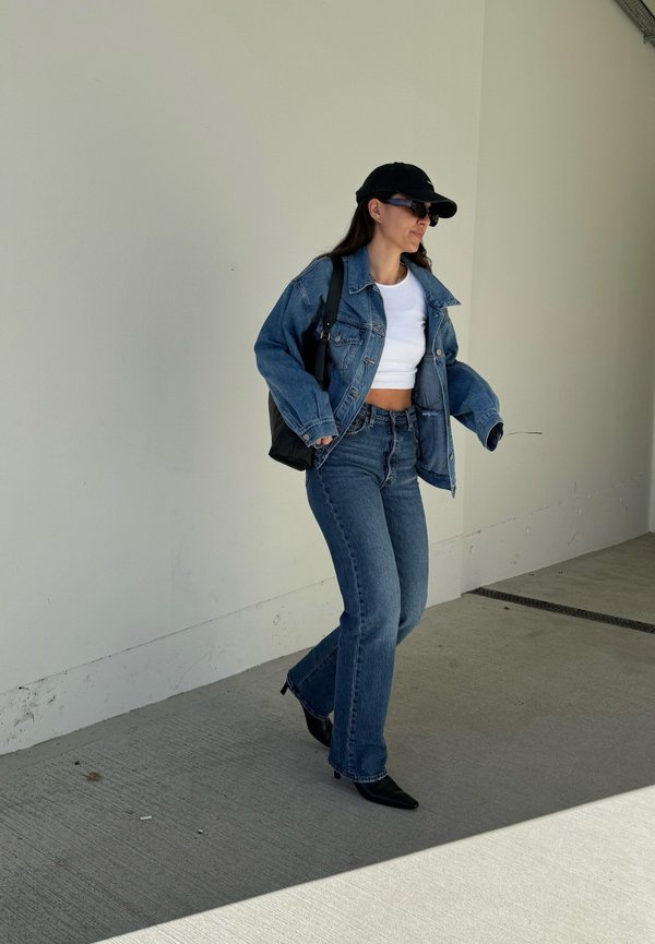 Denim jacketin päällä valkoinen crop top, yhdistettynä levenneisiin farkkuihin. Musta käsilaukku ja kärkitossut. Tummansininen baseball-lippis ja aurinkolasit käytössä.