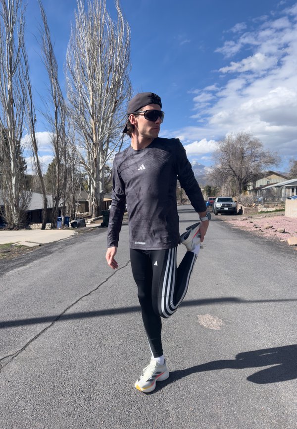 Atletiekoutfit: zwart langetermijnshirt met textuurontwerp, zwarte leggings met witte strepen, en hardloopschoenen met meerkleurige accenten.