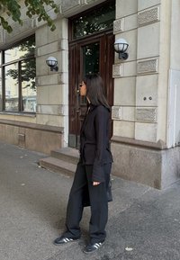 Juodas marškiniai su ilgomis rankovėmis, derinami su laisvais juodais kelnais ir juodomis sportinėmis bateliais su baltomis juostelėmis, miesto šaligatvyje.