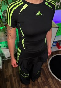 Must have musta mustab ja roheliste aktsentide ja triipudega must sportlik särk, millele on kombineeritud must alt osa laieneva disainiga. Materjal näib olevat veniv ja kerge.