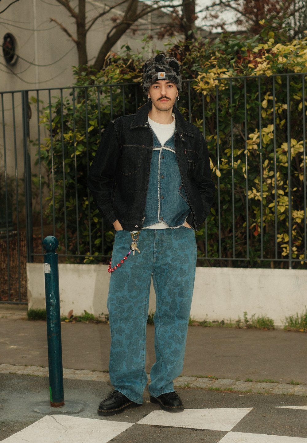 Veste en jean portée sur un gilet en jean bleu, associée à un jean bleu clair à motifs. Agrémentée d'un chapeau pelucheux et d'une chaîne avec une clé. Chaussures noires.