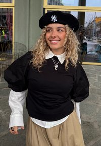 Svart skjorte med puffermet over en hvit skjorte med krage, kombinert med et beige skjørt. Inkluderer en svart beret med en hvit logo.