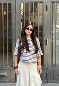 Stribet kortærmet top i hvid og marineblå, parret med en let nederdel med broderet detalje. Accessoriseret med solbriller og en brun taske.