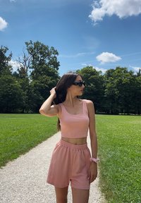Roze geribbelde crop top en bijpassende shorts met een elastische tailleband. De outfit is gecombineerd met een roze scrunchie en een zonnebril.