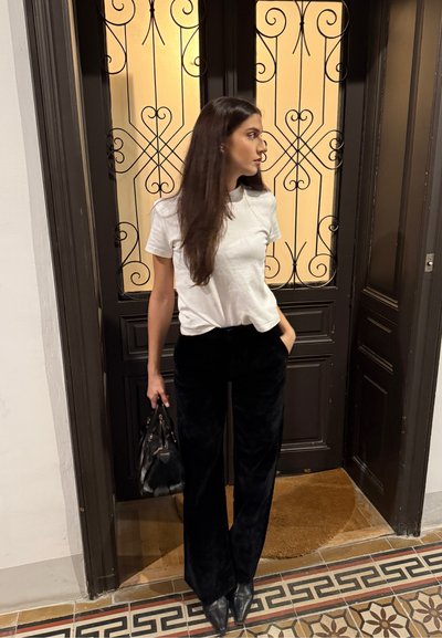 Pantalones anchos de terciopelo negro combinados con una camiseta blanca ajustada. El conjunto se completa con tacones negros puntiagudos y un bolso negro.