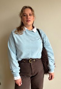 Hele sinise pikkade varrukatega särk valge kraega, kombineeritud pruunide kõrge vöökohaga pükstega. Must rihmaga kott lisab rõivastusele aktsendi. Sile tekstuur.