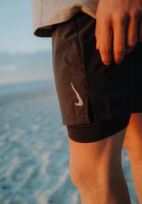 Crne sportske kratke hlače sivoj Nike logotipom s lijeve strane, sa pripijenim crnim slojem ispod i malim prorezom na rubu.