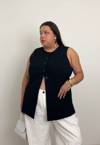 Melns bezrokains vestes tips ar pieciem pogām, ar sānu kabatām. Kombinēts ar baltām plaša piegriezuma biksēm. Aksesuārs - maza somiņa ar pērlītēm.