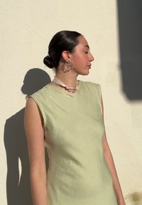 Light green sleeveless dress with a smooth texture, paired with oversized transparent earrings and a matching choker.