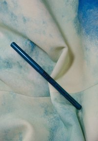 Liner mécanique bleu reposant sur un tissu doux et clair avec un motif bleu subtil. Présente une finition lisse et brillante ainsi qu'une lettrage clair.