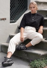 Sort oversized t-shirt, cremede bukser med opsmøg, og sorte sneakers. Lagde sølv halskæder, siddende på sten-trapper med grønne planter nedenfor.