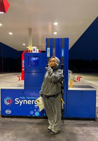 Pompa di benzina con design blu e rosso; il display digitale mostra 122,05 e 14,58; situata in una stazione di servizio al crepuscolo.