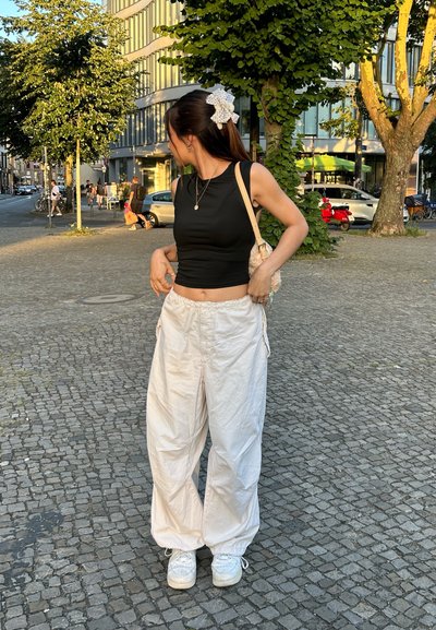 Pantalones anchos blancos, top negro corto y zapatillas blancas. También hay una bolsa de color claro con un patrón y un clip decorativo para el cabello.