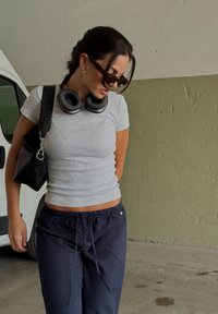Conjunto casual com uma t-shirt cinza justa com texturização, calças azul-marinho com cordão, mala preta de ombro e auscultadores de sobrecabeça.
