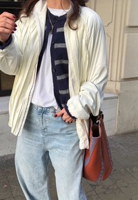 Fehér steppelt dzseki sötétkék csíkos kardigán felett, világoskék farmerral viselve. Barna és lila szegecselt táskát tart.