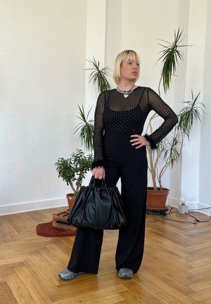 Top negro transparente de manga larga con puntos texturizados, pantalones negros de tiro alto y un gran bolso de cuero negro; detalles plateados y calzado casual.