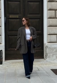 Överdimensionerad grå ullblazer över en vit crop top, matchad med vida mörkblå jeans och spetsiga svarta klackar. Svart handväska som accessoar.