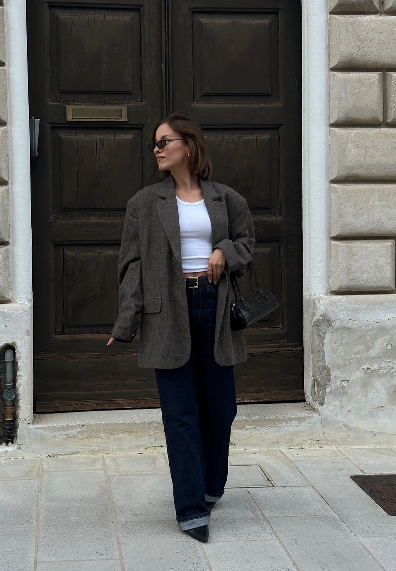 Oversized grey wool blazer worn over a white crop top, teamed with wide-leg dark denim jeans and pointed black heels. Complemented by a black handbag.