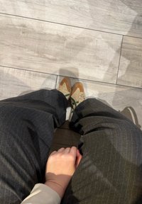 Chaussures bicolores beige et marron avec un accent vert, assorties à un pantalon à rayures fines foncé, vues depuis une position assise.