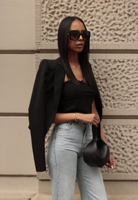 Črni skrajšani blazer preko črnega topa, svetlo modri hlače visoke pasu in črna torbica. Velika kvadratna sončna očala in ravno gladki lasje.