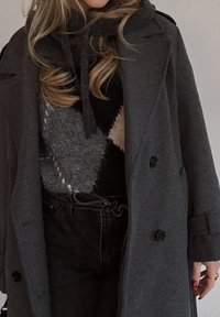 Manteau en laine grise à double boutonnage, associé à un pull noir avec un motif géométrique gris et crème, et un jean noir taille haute.