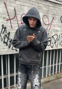 Grey zip-up hoodie with a drawstring hood and textured panels, teamed with distressed dark jeans that feature rips and a keychain.