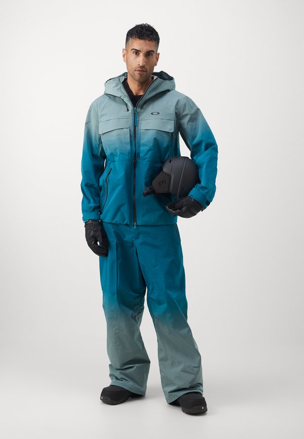 Chaqueta de nieve en degradado verde azulado con capucha, cierre de cremallera en el frente y dos bolsillos en el pecho, combinada con pantalones a juego y casco negro. Guantes y zapatos texturizados.