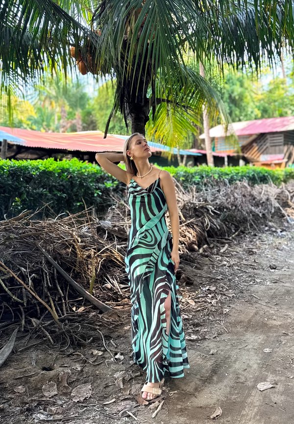 Robe longue à imprimé zèbre vert et noir, en tissu léger, avec une silhouette fluide et des fentes latérales. Des sandales complètent le look.