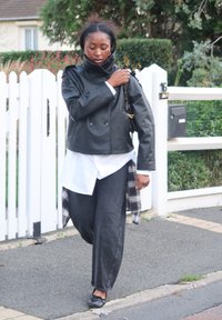 Sort skinnjakke med høy krage, hvit skjorte og løse svarte jeans, kombinert med svarte ballerinasko og en rutete flanellskjorte knyttet rundt livet.