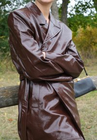 Marron trench coat en cuir vernis avec un design à double boutonnage, un large col et une texture douce et brillante ; assorti d'un petit sac à main noir.