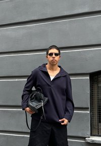 Maglione blu navy con colletto, tessuto texture, indossato su una canotta bianca, abbinato a pantaloni corti neri e con una borsa nera in mano.