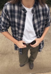 O cămașă în carouri albastru închis și alb peste un tricou alb, asortată cu pantaloni verde măsliniu și cizme gri, având o curea închisă la culoare cu o cataramă argintie.