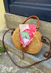 Borsa a mano rotonda in vimini naturale con manico in pelle, con foderatura in tessuto a motivo rosa e confezione di prodotti di bellezza all'interno.