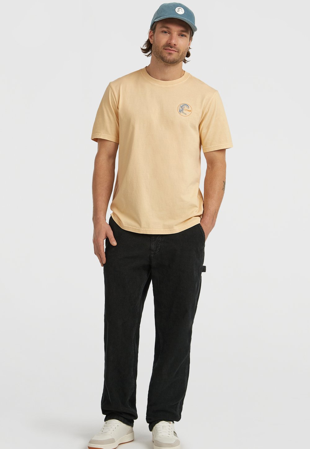 Ljusgul t-shirt med kort ärm och en cirkulär logotyp, ihopparad med svarta byxor och vita sneakers. Hatet är blått med en logotyp.