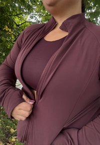 Maroon zip-up jacket with a high collar, layered over a matching vest top. Smooth fabric with a fitted design and thumbholes in the sleeves.