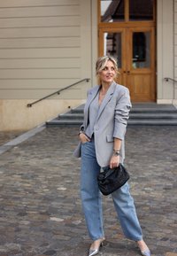 Svetlo sivo prugasto sako preko sive bluze, uparen s svetloplavim širokim farmerkama i srebrnim cipelama sa špicastim prstima. Drži crnu tkanu torbu.