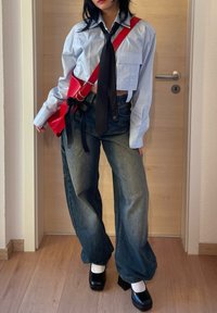 Camicia azzurra croppata con bottoni e cravatta nera, jeans a vita alta in denim scuro a gamba larga, borsa rossa a tracolla e scarpe piattaforma nere.