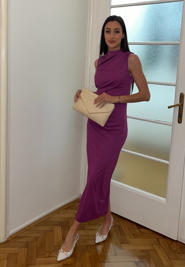 Mujer con un vestido midi morado sin mangas, sosteniendo un bolso de mano beige, de pie cerca de una puerta blanca con paneles de vidrio esmerilado.